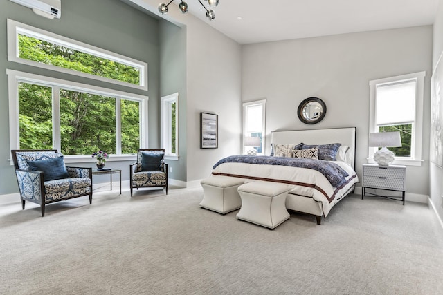 carpeted bedroom with a towering ceiling, a wall mounted AC, and a notable chandelier