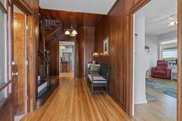 corridor featuring wooden walls, light hardwood / wood-style flooring, and a notable chandelier