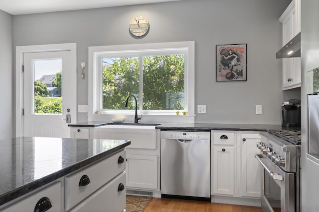 kitchen featuring dark stone countertops, appliances with stainless steel finishes, wall chimney exhaust hood, and white cabinets