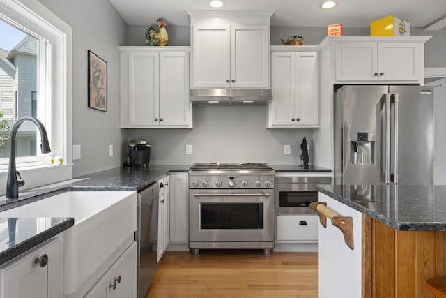 kitchen featuring sink, white cabinetry, light hardwood / wood-style flooring, appliances with stainless steel finishes, and dark stone counters