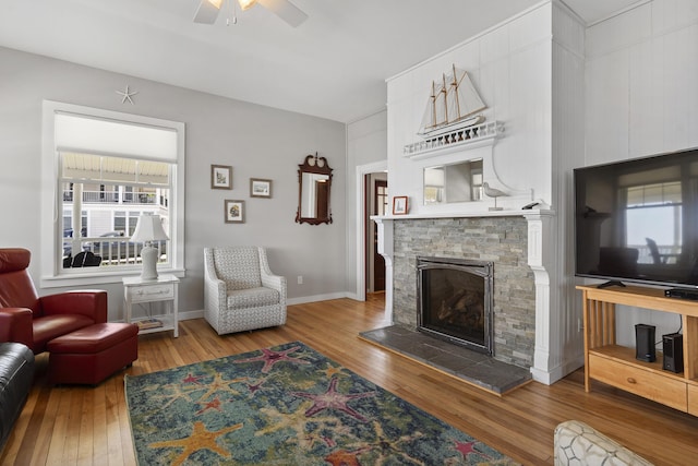 living room with hardwood / wood-style flooring, a stone fireplace, and ceiling fan