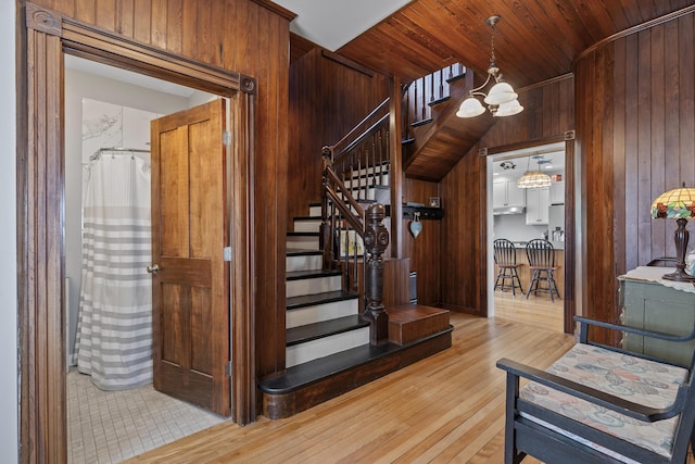 staircase with wood-type flooring, wooden ceiling, a chandelier, and wood walls