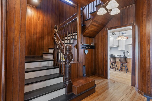 stairway with hardwood / wood-style flooring, wooden walls, and a chandelier