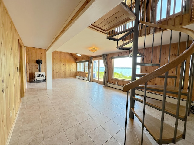 interior space with a baseboard heating unit, wood walls, a wood stove, a water view, and light tile patterned floors