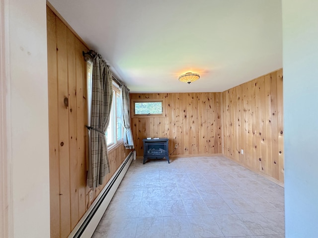 unfurnished room with a wood stove, a baseboard radiator, and wooden walls