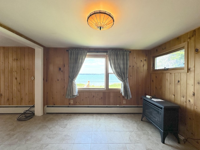 spare room with a water view, baseboard heating, a wood stove, and wooden walls