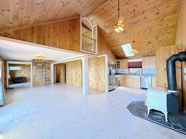 kitchen featuring a skylight, wood walls, appliances with stainless steel finishes, a wood stove, and light brown cabinetry