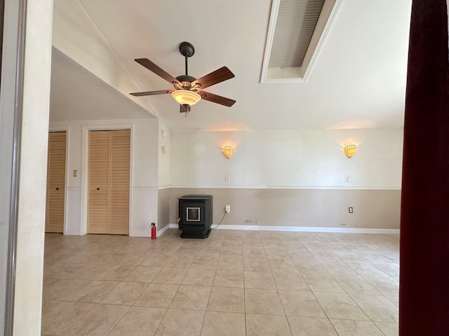 tiled empty room with ceiling fan, a wood stove, and lofted ceiling