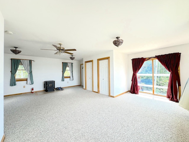 unfurnished living room with ceiling fan, a wood stove, and carpet