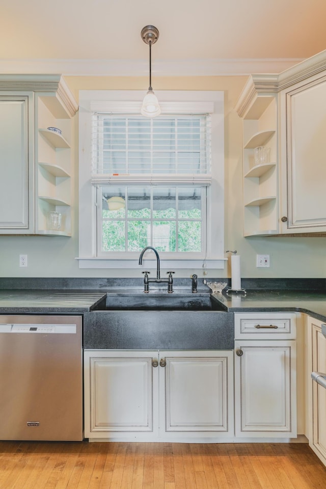 kitchen with light hardwood / wood-style floors, cream cabinetry, hanging light fixtures, stainless steel dishwasher, and sink