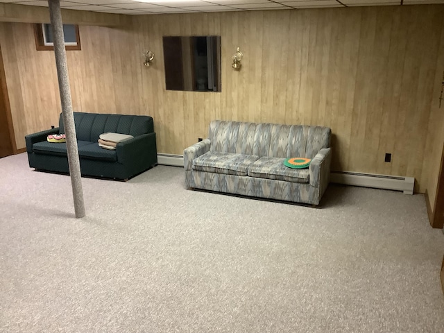 basement with a baseboard heating unit, a paneled ceiling, wood walls, and light carpet