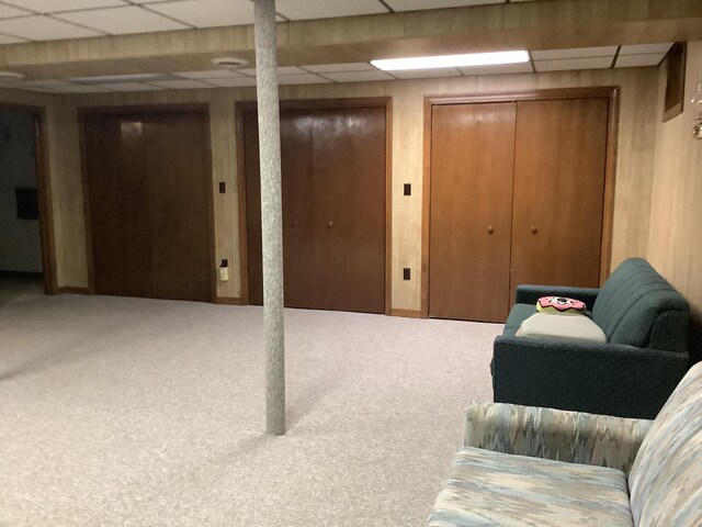 basement featuring carpet, a drop ceiling, and wood walls