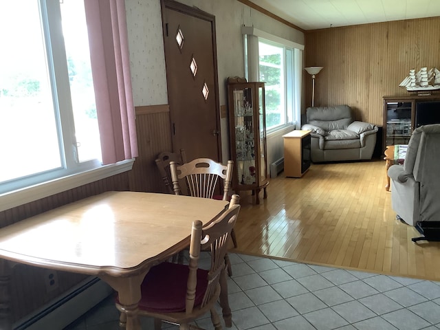 dining room featuring baseboard heating, light tile patterned flooring, and wood walls