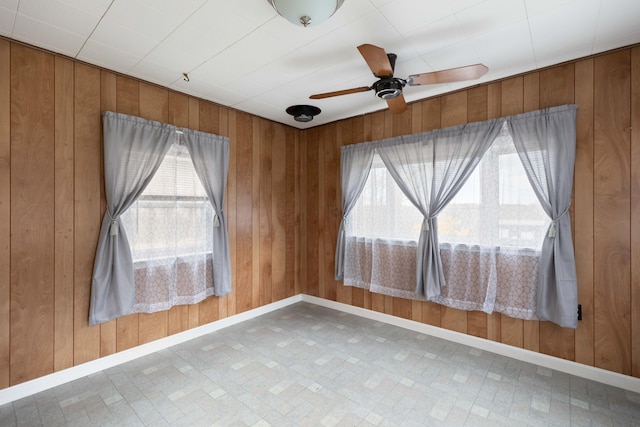 spare room with ceiling fan, wooden walls, and baseboards