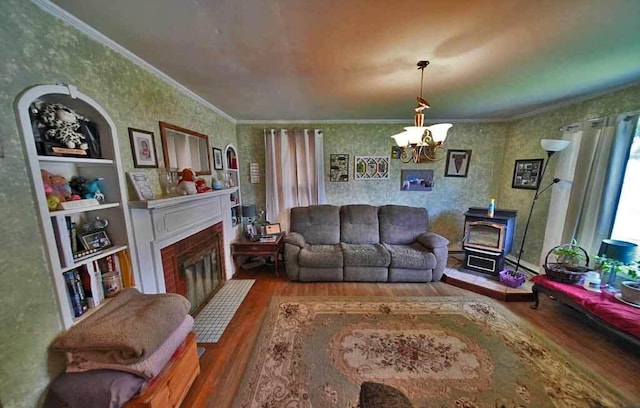 living room with a wood stove, crown molding, built in shelves, a notable chandelier, and wood-type flooring