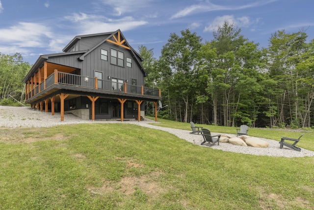 rear view of property featuring board and batten siding, an outdoor fire pit, a lawn, and a wooden deck