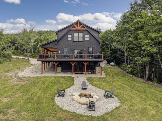 rear view of property featuring a forest view, an outdoor fire pit, a lawn, and a wooden deck