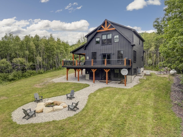 back of house featuring a lawn, board and batten siding, an outdoor fire pit, a patio area, and a wooden deck