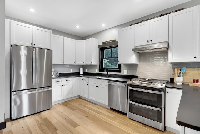 kitchen with dark countertops, appliances with stainless steel finishes, white cabinets, a sink, and under cabinet range hood