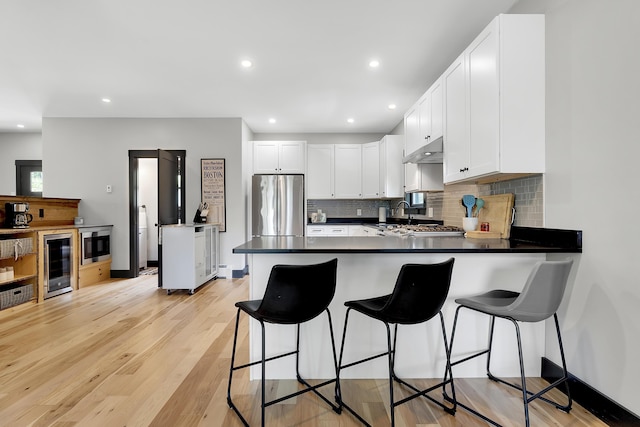 kitchen with appliances with stainless steel finishes, beverage cooler, white cabinetry, and under cabinet range hood