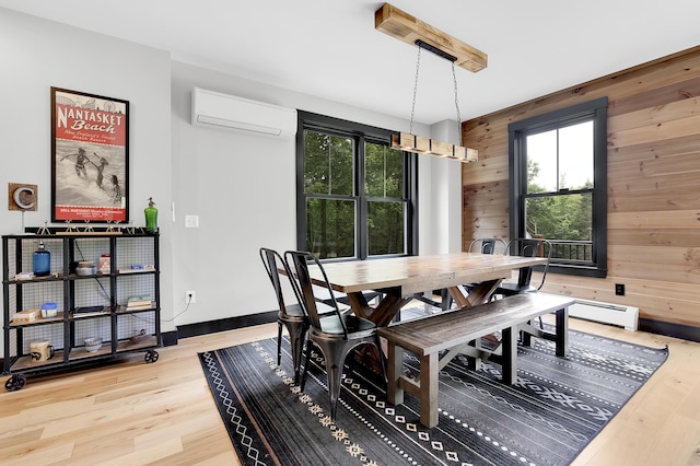 dining space with wood walls, baseboards, an AC wall unit, baseboard heating, and light wood finished floors