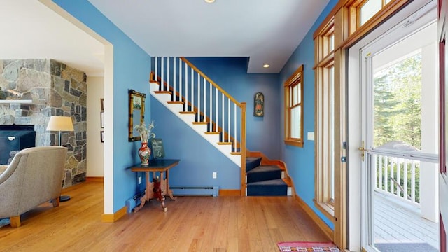 entrance foyer with light wood-type flooring, a baseboard radiator, and a stone fireplace