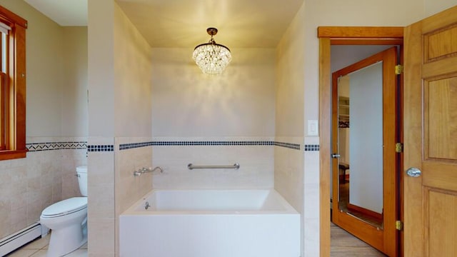 bathroom featuring a washtub, a baseboard radiator, a notable chandelier, toilet, and tile walls