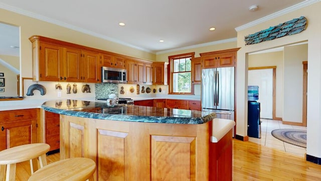 kitchen with stainless steel appliances, ornamental molding, dark stone counters, a kitchen island, and light wood-type flooring