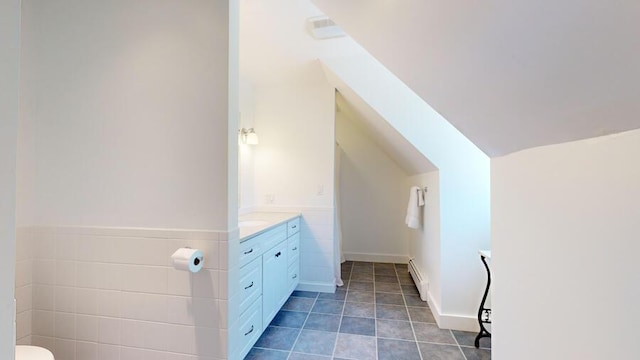 bathroom with vanity, lofted ceiling, tile patterned floors, baseboard heating, and tile walls