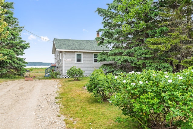 view of side of property featuring a shingled roof, a chimney, and dirt driveway