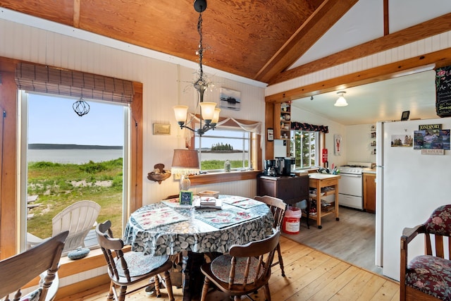 dining space with a water view, lofted ceiling, an inviting chandelier, and light hardwood / wood-style floors