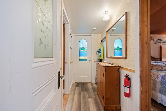 doorway to outside with wood finished floors and wallpapered walls