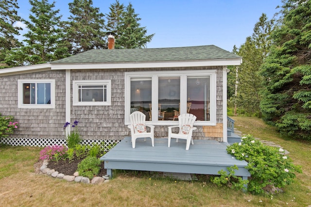 rear view of house featuring a shingled roof, a deck, and a lawn