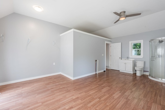 interior space with baseboards, ceiling fan, a sink, light wood-style floors, and vaulted ceiling