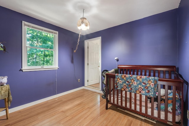 bedroom with a crib, baseboards, and wood finished floors