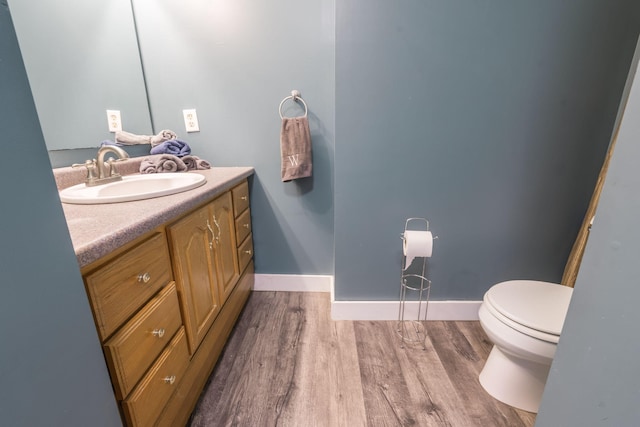half bathroom featuring toilet, wood finished floors, baseboards, and vanity