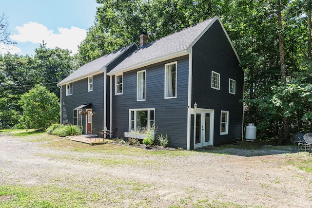 colonial-style house featuring a chimney and roof with shingles