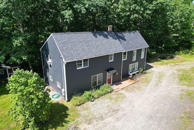 exterior space with dirt driveway, roof with shingles, and a chimney