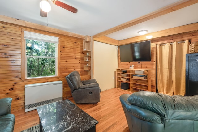 living room with heating unit, wood finished floors, wood walls, beamed ceiling, and ceiling fan