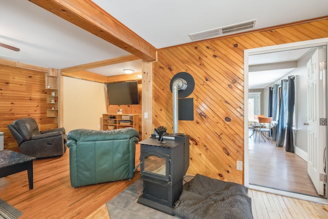 living area featuring wood walls, visible vents, beamed ceiling, wood finished floors, and a wood stove
