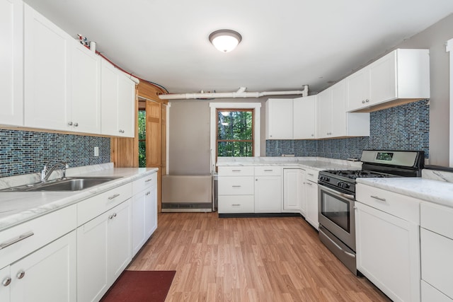 kitchen featuring a sink, stainless steel gas range, white cabinetry, tasteful backsplash, and light wood-style flooring