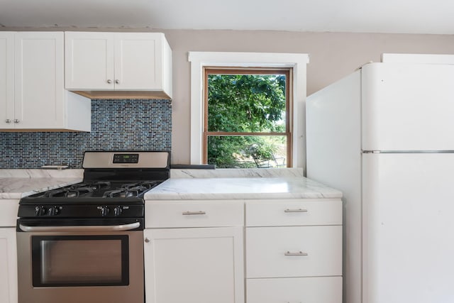kitchen with tasteful backsplash, stainless steel range with gas cooktop, light stone counters, freestanding refrigerator, and white cabinets