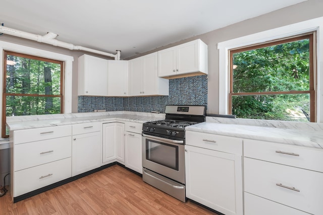 kitchen featuring light wood-style flooring, light stone countertops, tasteful backsplash, stainless steel range with gas cooktop, and white cabinetry
