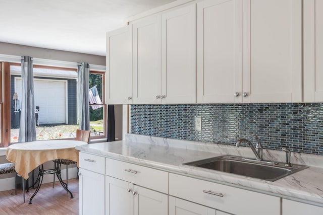 kitchen with white cabinets, light wood-style flooring, decorative backsplash, and a sink
