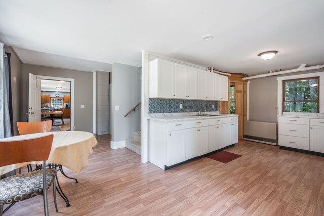 kitchen featuring light countertops, white cabinetry, a sink, light wood-style floors, and backsplash