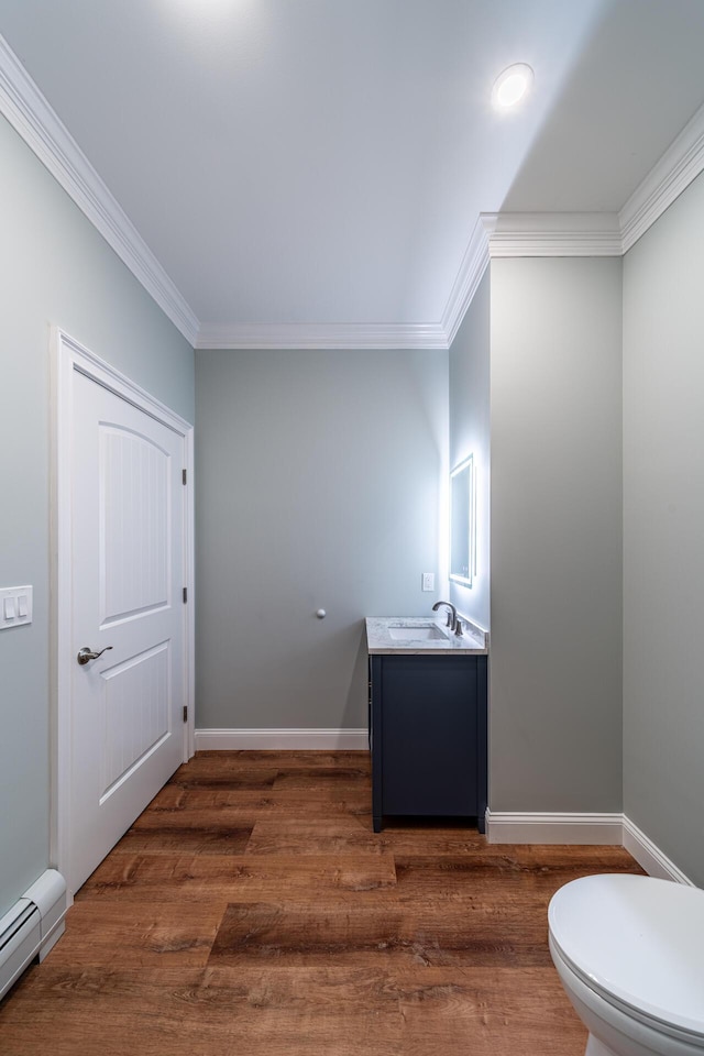 bathroom with ornamental molding, vanity, baseboard heating, wood-type flooring, and toilet