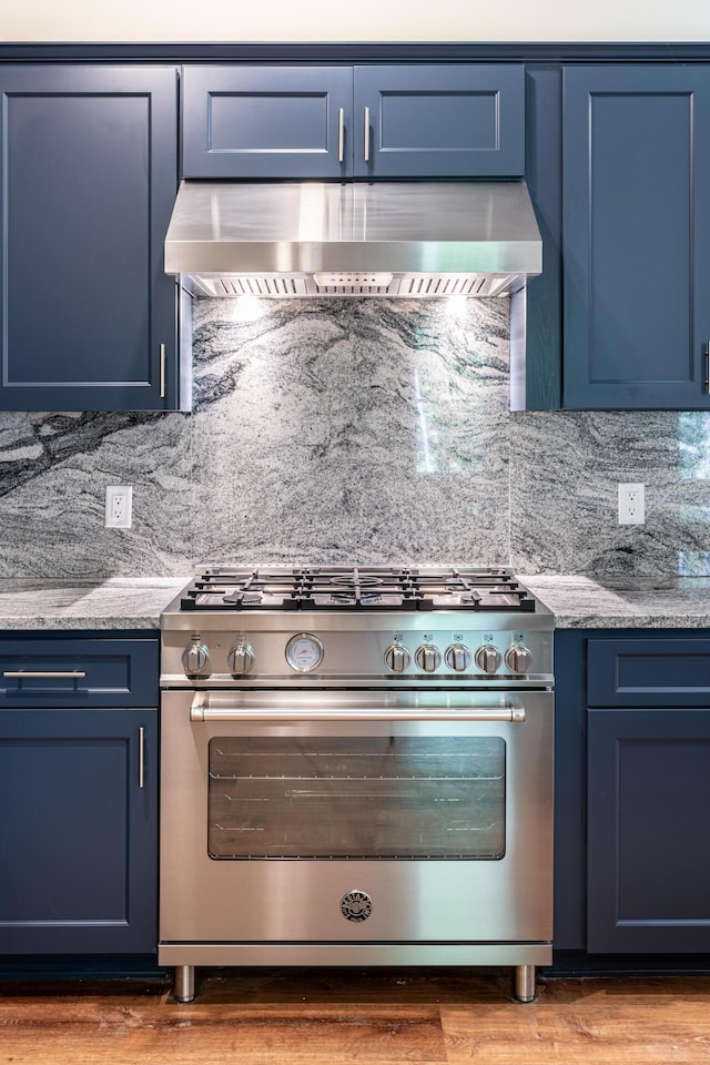 kitchen featuring designer stove, blue cabinets, tasteful backsplash, and wall chimney exhaust hood