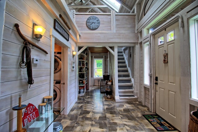 foyer entrance featuring wood walls, stacked washer and clothes dryer, and lofted ceiling with skylight