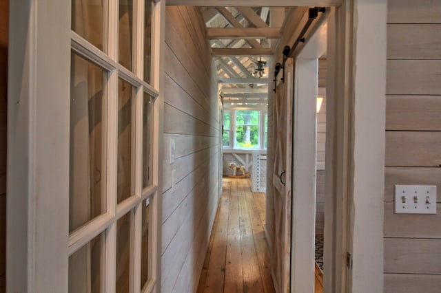 hallway with hardwood / wood-style floors, wood walls, and a barn door