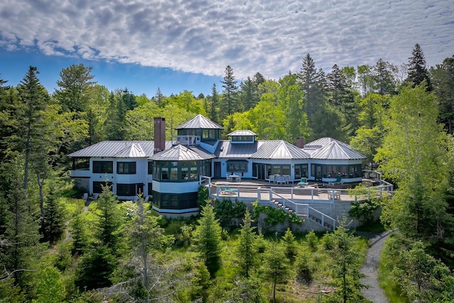 rear view of property featuring a standing seam roof, a chimney, a wooded view, and an outdoor pool